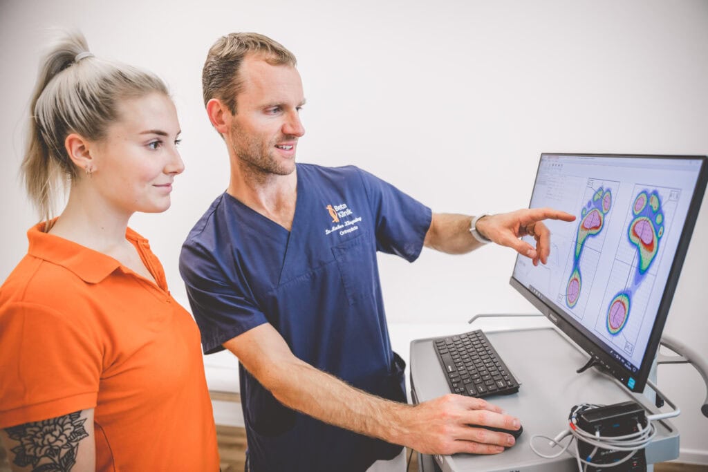 Orthopäde erklärt der medizinischen Fachangestellten für Orthopädie etwas an einem Computer.