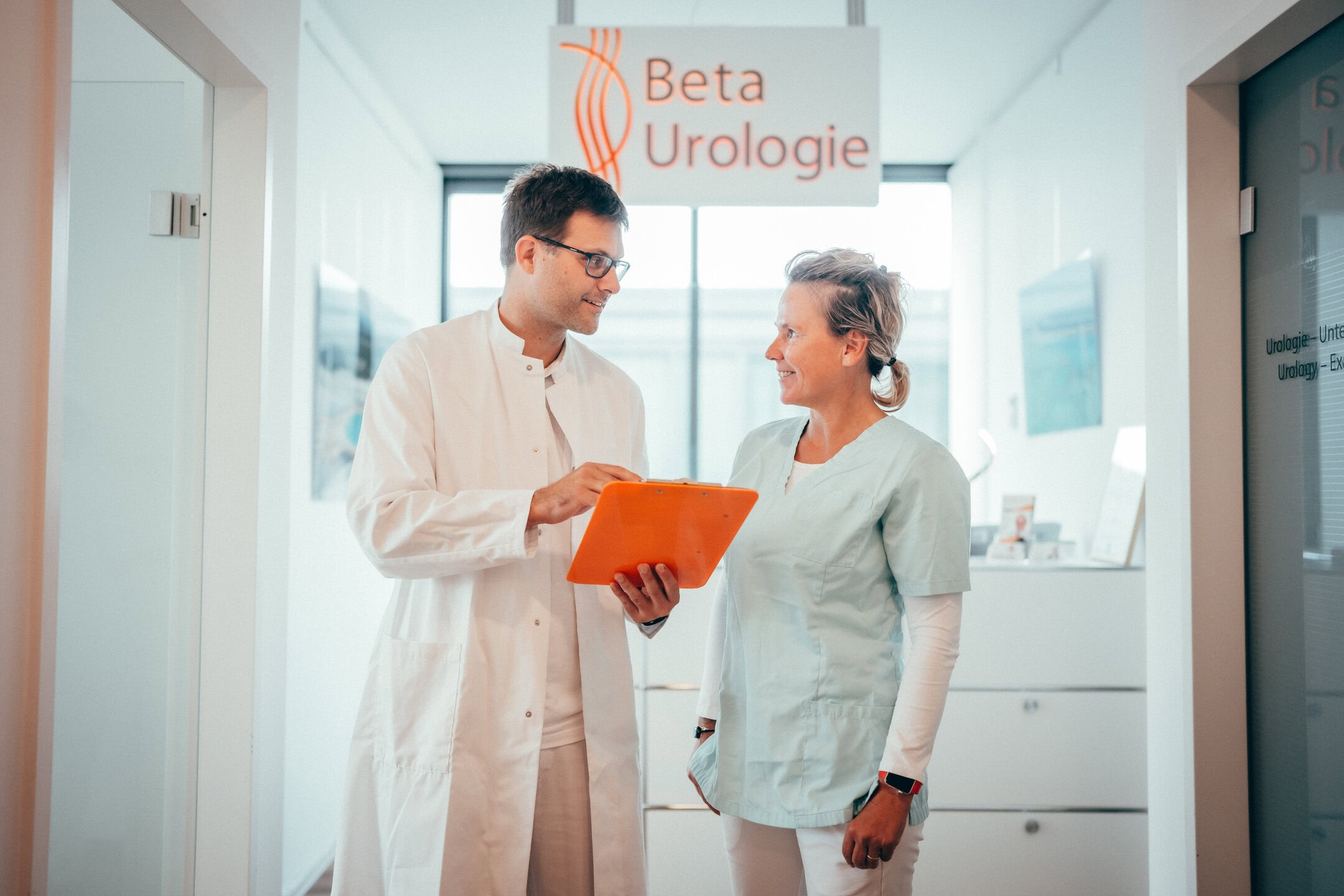 Arzt der Urologie und eine Mitarbeiterin am Empfang sprechen miteinander.