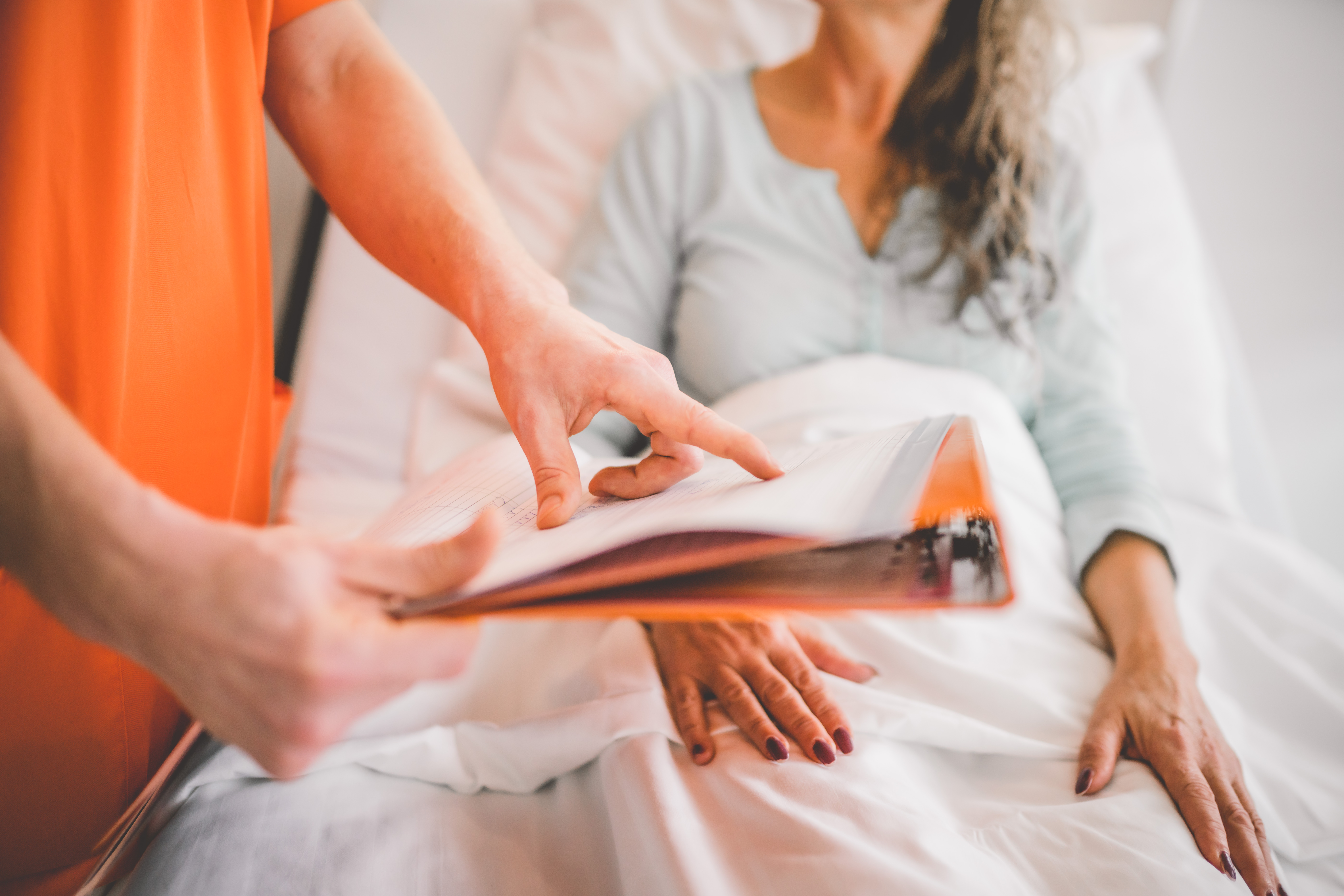 Medizinischer Fachangestellter erklärt einer Patientin etwas und zeigt dabei auf ein Klemmbrett.