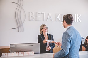 Mann übergibt Patientenbogen der Rezeptionistin