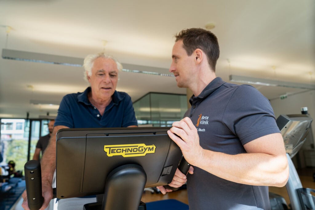 Patient sitz auf Ergo-Bike und wird dabei von Physiotherapeut betreut