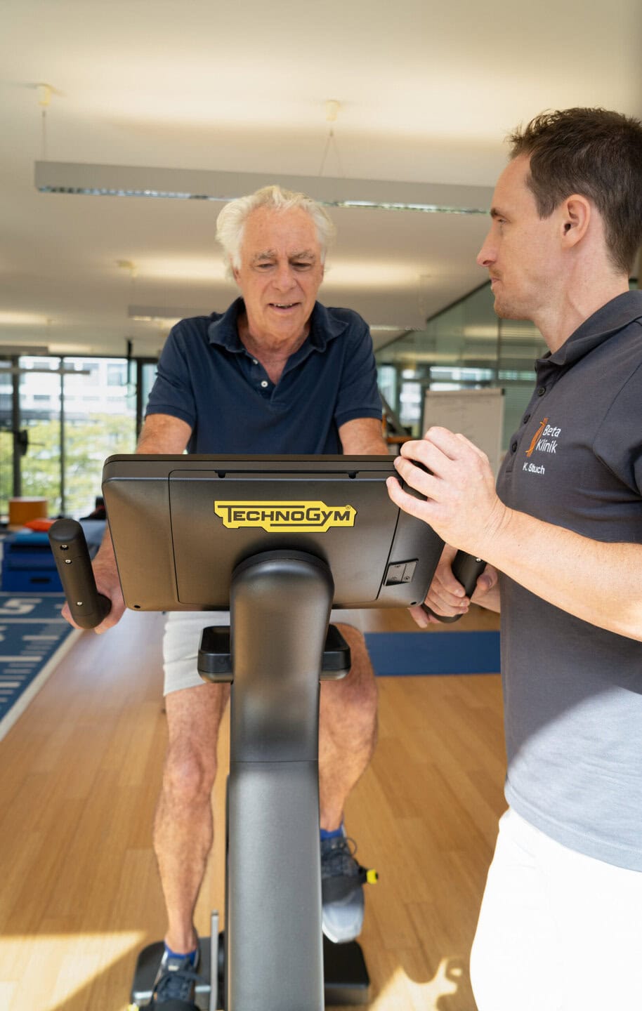 Patient fährt auf einem Ergo Bike und wird dabei von Physiotherapeut betreut