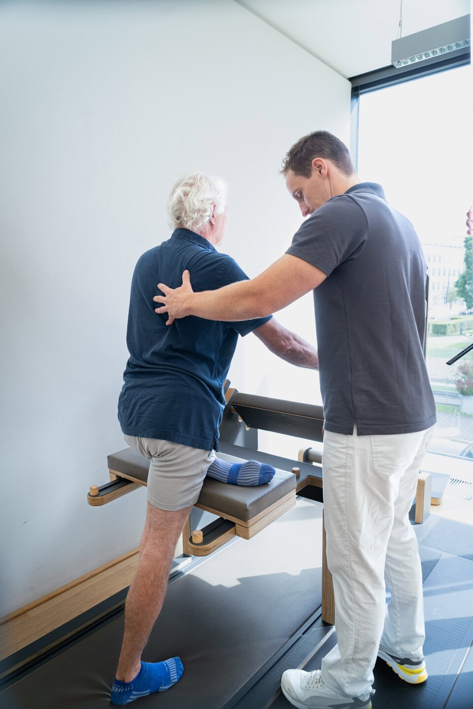 Patient trainiert seinen Unterkörper an einem Gerät des Five-Beweglichkeit-Parcours und wird vom Physiotherapeuten betreut