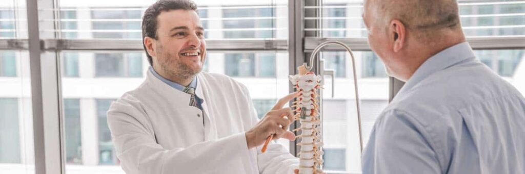 Facharzt Igressa zeigt Patienten Wirbel an einem Modell der Wirbelsäule.